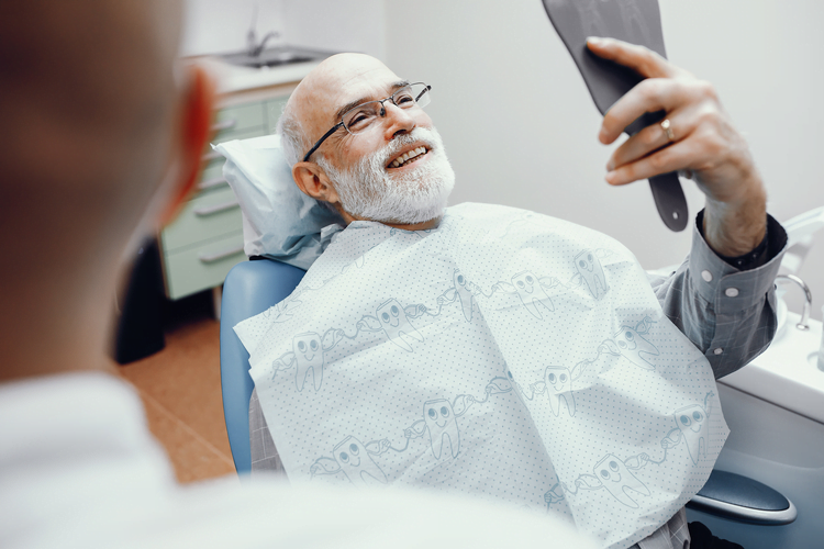 hombre en silla de dentista sosteniendo un espejo para mirarse los dientes